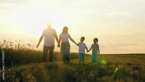 Son daughter dad mom walk hand in hand in child. Children dream, complete family, kids. Happy family of farmers with children walks through wheat field, sunset. Big family, group of people in nature.