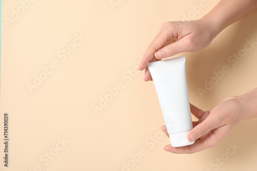 Woman with tube of hand cream on beige background, closeup. Space for text