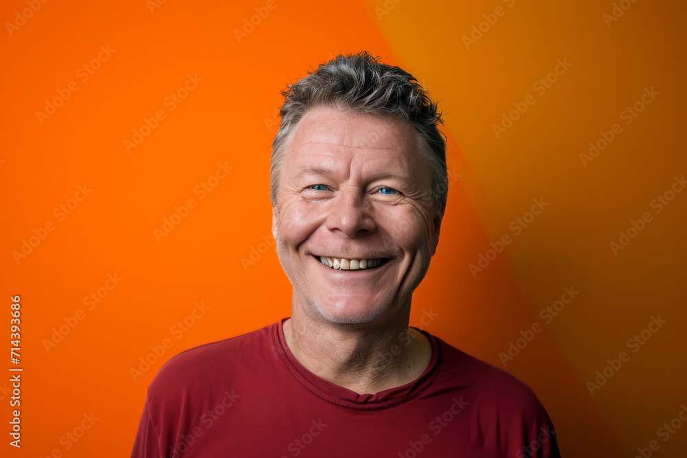 A man in a red shirt is smiling in front of an orange background A man in a red shirt is smiling in front of an orange background