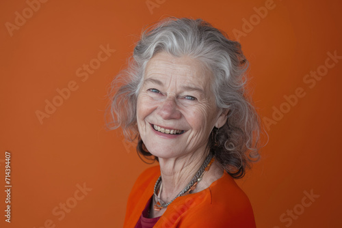 A woman with gray hair is smiling in front of an orange background