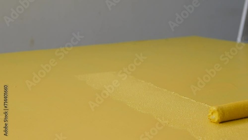 painting a yellow wall with a roller.