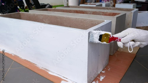 A woman's hand wearing a glove and using a red paintbrush is painted white on a plaster pot.