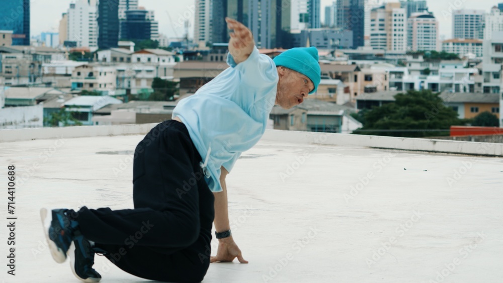 Professional caucasian B-boy dancer practicing street dancing at rooftop with city or urban. Motion shot of young man performing street dance by doing freeze pose. Outdoor sport 2024. Endeavor.