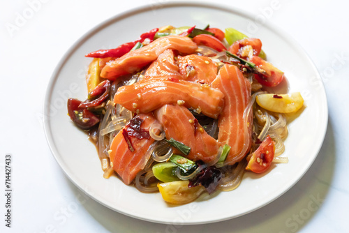 Spicy salad with fresh salmon and potato noodles mixed fermented fish sauce on white plate.