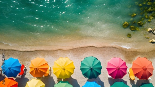 Overhead shot of a beach scene with multicolored umbrellas lined along the shore.