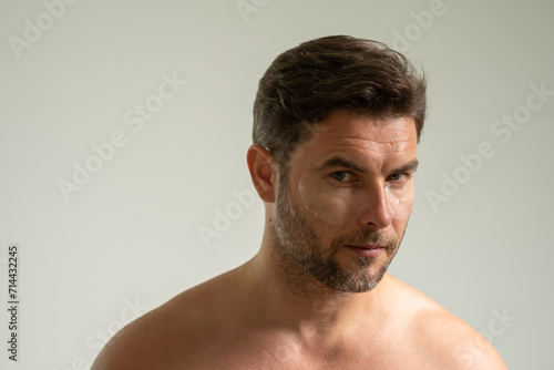 man with healthy skin. Head shot portrait smiling American young man with naked shoulders checking wrinkles or acne on forehead, looking at camera, facial cosmetology, treatment, skincare concept