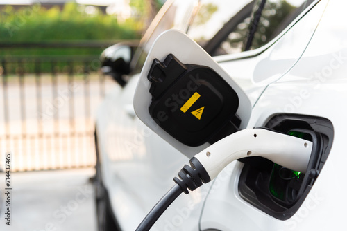 An electric vehicle, charged by alternative clean energy and plugged in with a cable from a home charging station, stands as a symbol of progressive thinking