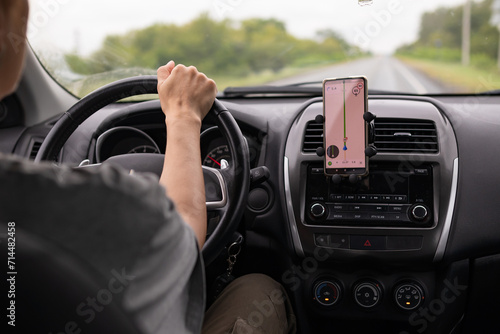 Rear view of a young traveler using a navigator on a mobile phone behind the wheel of a modern car .