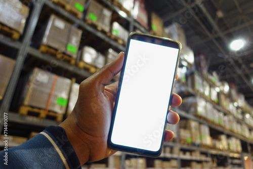 business owner holding phone mock up in warehouse.