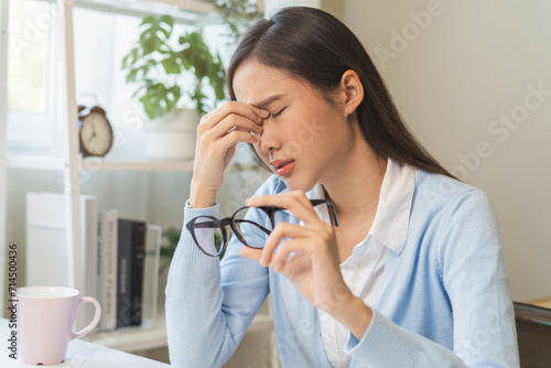 Exhausted  asian young business woman working at office desk  took off eye glasses  massage rubbing nose from dry eyes  suffer on work hard  using laptop computer at office home  problem overtime job.
