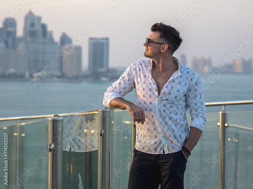 Handsome man standing on the empty deck of a cruise liner against the background of the city of Doha. Sunny morning, clear day. Closeup, outdoor. Vacation and travel concept