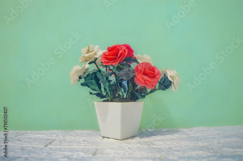 A decorative plastic fake flower bouquet in a white flower vase against a turquoise green wall background
