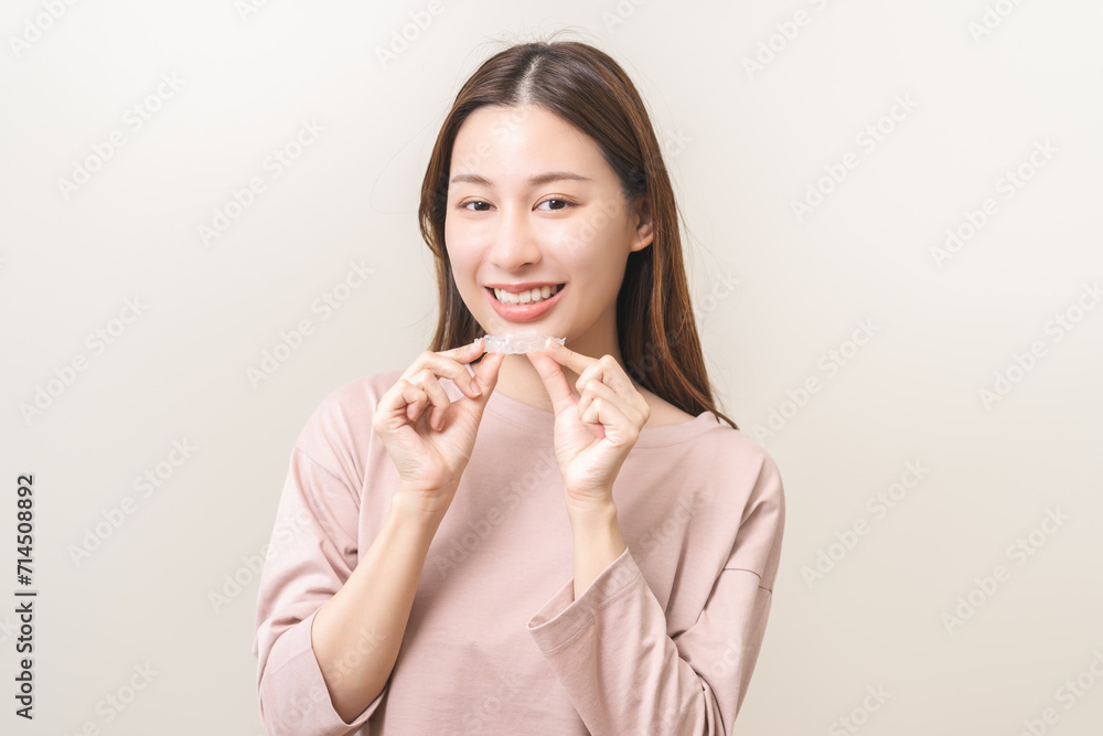Dental invisible braces, beautiful smiling asian young woman holding invisalign braces, wearing orthodontic silicone trainer, white smile using invisible whitening tray. Stomatology, dental healthcare Dental invisible braces, beautiful smiling asian young woman holding invisalign braces, wearing orthodontic silicone trainer, white smile using invisible whitening tray. Stomatology, dental healthcare