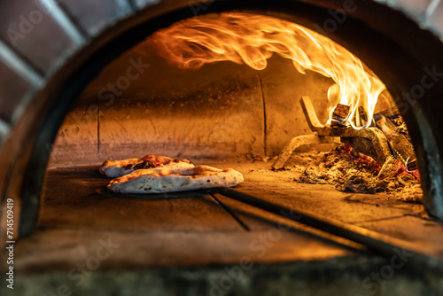 Traditional oven for baking pizza with burning wood and shovel. The cook rotates the pizza in the oven to ensure even baking