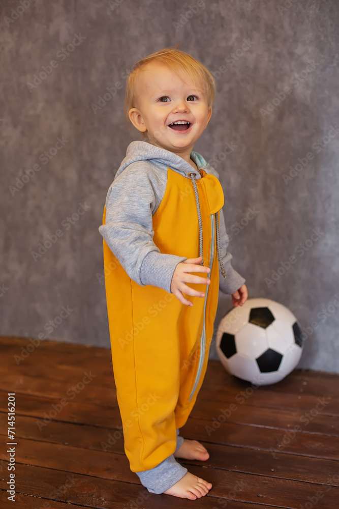 A happy little boy in a yellow and gray jumpsuit is lying next to a soccer ball A happy little boy in a yellow and gray jumpsuit is lying next to a soccer ball