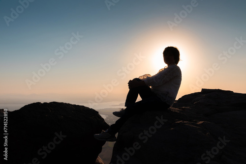 Silhouette Thai woman sitting on a rock on the mountain Amidst beautiful views And the sunrise background in the morning. freedom and travel concept.