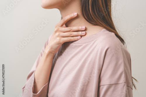 Sickness in inflaming asian young woman, girl use hand check self touch at sore throat, pain thyroid gland on neck or disease reflux, acid of suffer people on wall background. Medical and healthcare. photo