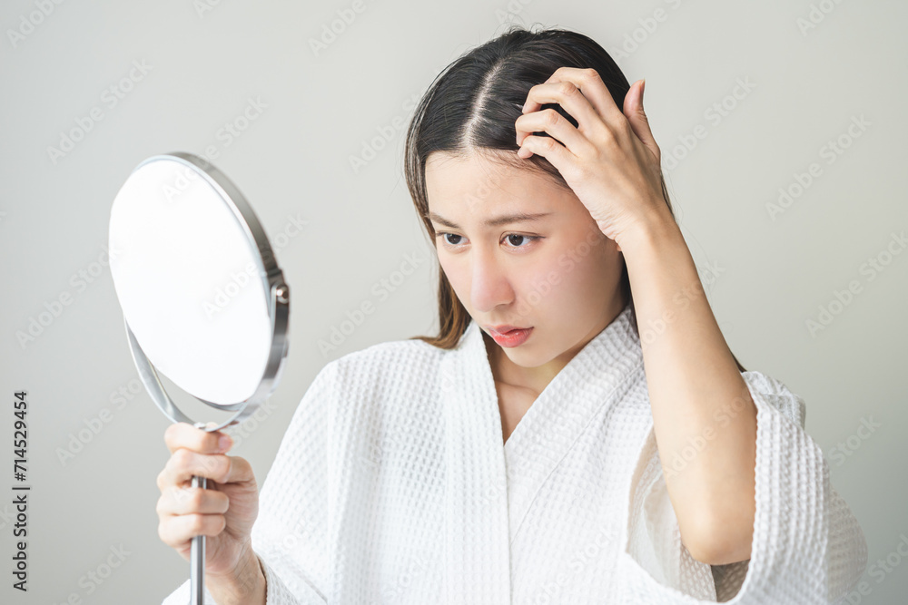 Damaged Hair symptom, face serious asian young woman, girl worry about balding, looking at scalp in mirror, hand in break into front hair loss, thin problem. Health care treatment for beauty concept. Damaged Hair symptom, face serious asian young woman, girl worry about balding, looking at scalp in mirror, hand in break into front hair loss, thin problem. Health care treatment for beauty concept.