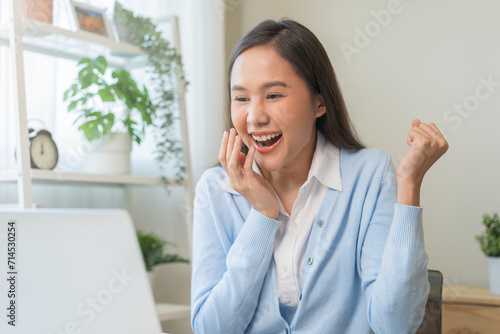 Excited with computer, happy celebrating success asian young woman, girl amazed looking good news at pc, laptop on desk at home office, get win online lottery, student winner celebrating achievement.