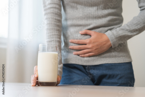 Pain, suffering asian young woman having a stomachache, abdominal pain or digestive, hand in holding belly after drink glass of milk. Lactose intolerance, allergy from dairy food, health care problem. photo