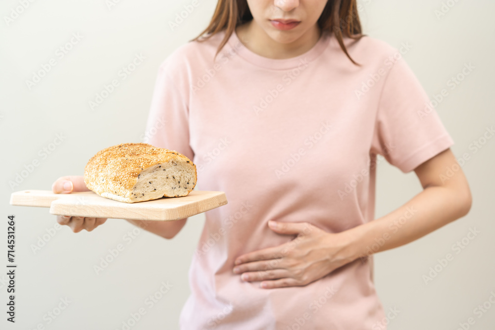 Gluten allergy, asian young woman hand holding, refusing to eat white loaf slice on board in breakfast food meal at home, girl having a stomach ache. Gluten intolerant and Gluten free diet concept. Gluten allergy, asian young woman hand holding, refusing to eat white loaf slice on board in breakfast food meal at home, girl having a stomach ache. Gluten intolerant and Gluten free diet concept.