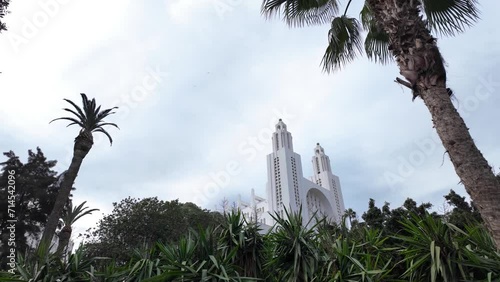 Famous Casablanca Cathedral, Ancienne église du Sacré-Cœur de Casablanca in a public garden covered with palm trees. The sky is cloudy.