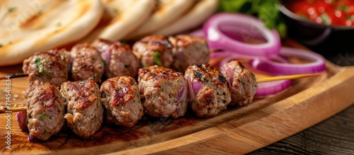 Close-up view of meat kebabs, served on a wooden board with pita bread, red onion rings, and sauce