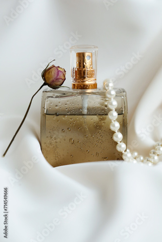 glass perfume bottle with delicate lilac flowers on a textured surface lit by the sun. Top view