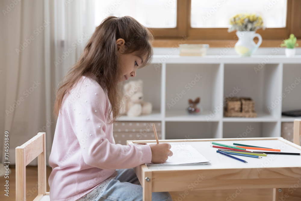 Little focused girl sit at table drawing pictures looks engrossed in painting process in sketchbook, cute preschooler kid spend leisure in cozy nursery, enjoy creative hobby, develop fine motor skills Little focused girl sit at table drawing pictures looks engrossed in painting process in sketchbook, cute preschooler kid spend leisure in cozy nursery, enjoy creative hobby, develop fine motor skills