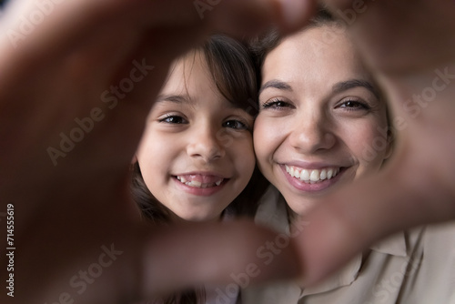 Close up faces, little girl and loving mother look at camera, make heart sign from joined fingers, bloggers share love with subscribers, dental services advertisement, happy motherhood, family ties