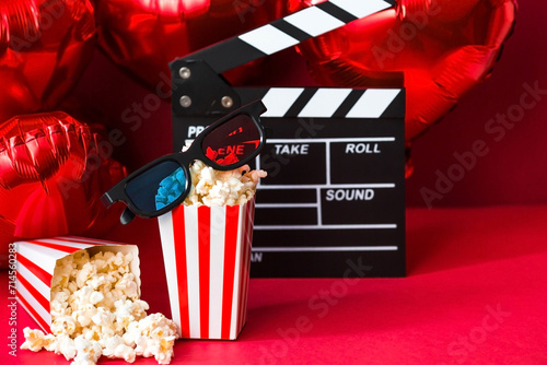 A banner for the film industry. A romantic movie date. A movie camera, 3D glasses, popcorn and heart-shaped foil balloons on a red background. The premiere of the film is on Valentine's Day.