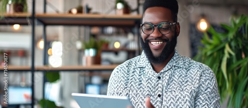Happy bearded black businessman using digital tablet and mobile app to manage business remotely at office.