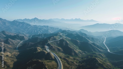  an aerial view of a winding road in a mountainous area with a mountain range in the distance in the distance is a bird's eye view of the road.