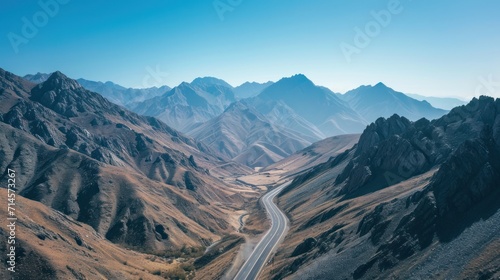  an aerial view of a mountain range with a road winding through the center of the mountain range in the foreground is a blue sky with a few clouds in the foreground.