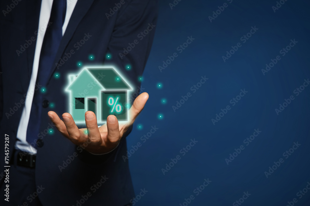 Mortgage rate. Man holding virtual house with percent sign on dark blue background, closeup. Space for text Mortgage rate. Man holding virtual house with percent sign on dark blue background, closeup. Space for text