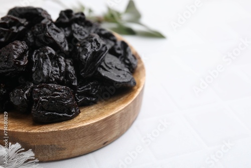 Sweet dried prunes on white tiled table, closeup. Space for text
