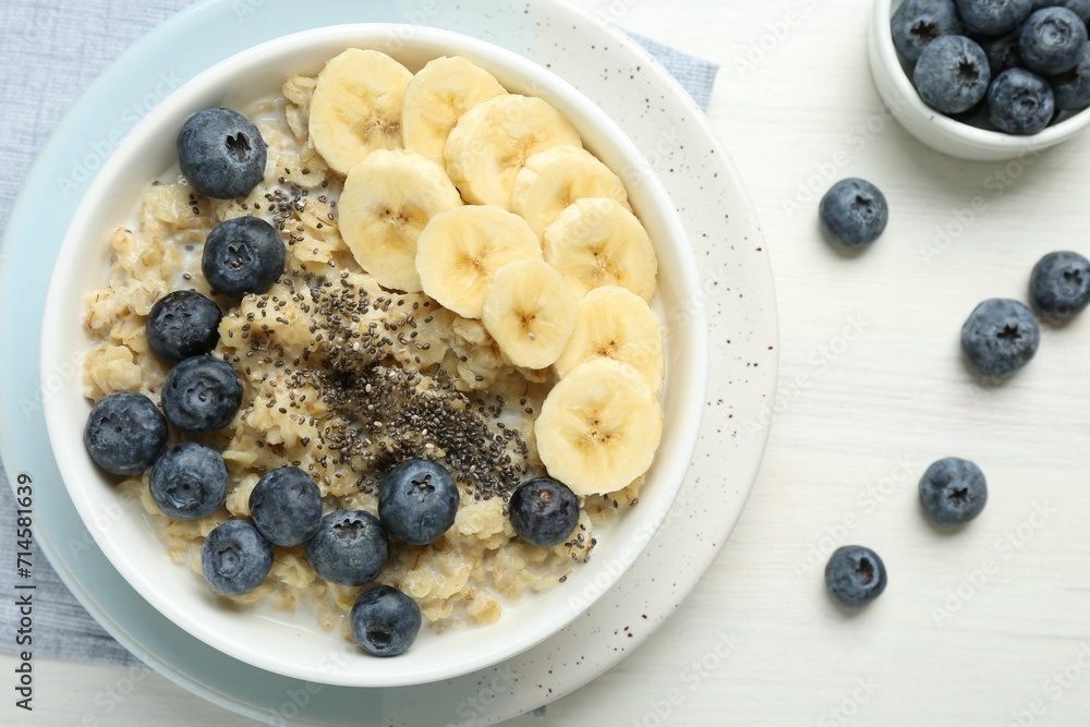 Tasty oatmeal with banana, blueberries and chia seeds served in bowl on white wooden table, flat lay Tasty oatmeal with banana, blueberries and chia seeds served in bowl on white wooden table, flat lay