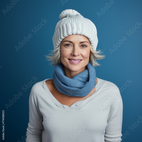 Happy middle aged woman in a white winter hat and a beige sweater. Portrait of beautiful mature woman in a winter cap smiling on a blue background looking at camera. Cheerful caucasian woman in a hat.