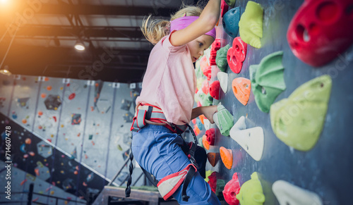 A strong baby climber climbs an artificial wall with colorful grips and ropes. photo