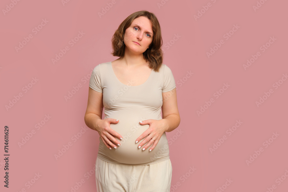A tired pregnant woman on a pink studio background. Pregnancy in a exhausted woman with a belly A tired pregnant woman on a pink studio background. Pregnancy in a exhausted woman with a belly