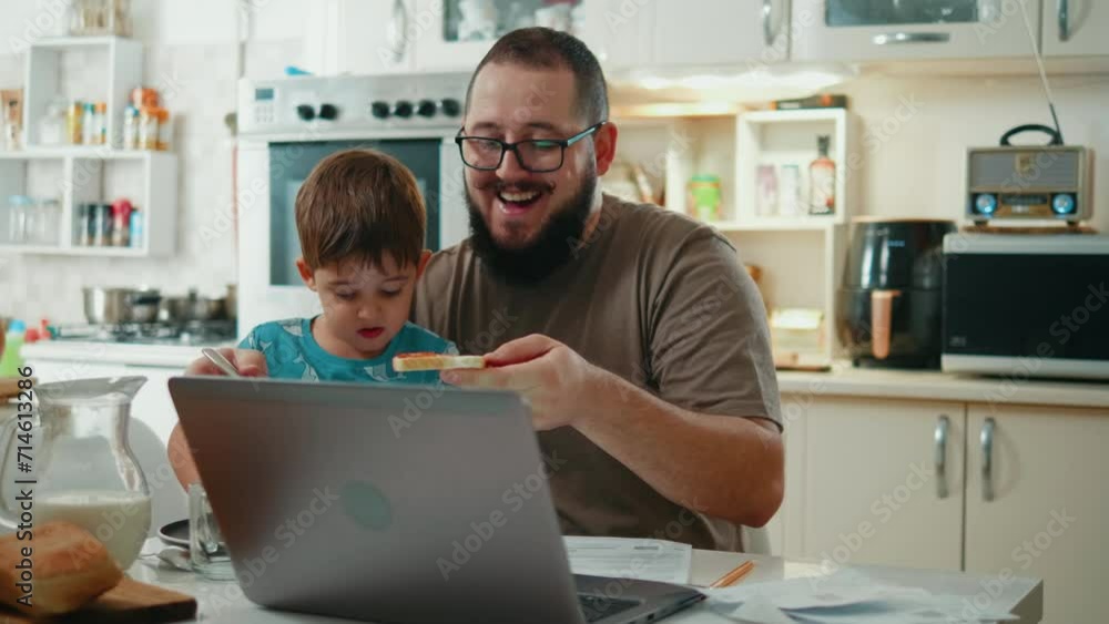 Father and little son are having breakfast together in the kitchen with a laptop and a mobile phone Father and little son are having breakfast together in the kitchen with a laptop and a mobile phone