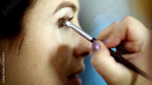 visagiste hand blends eyeshadow with brush on upper lid of model. photo