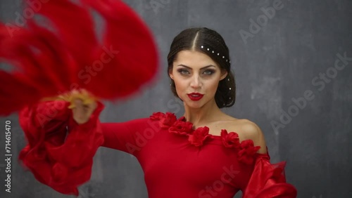 Young girl dancer dressed in red dress with fan poses.