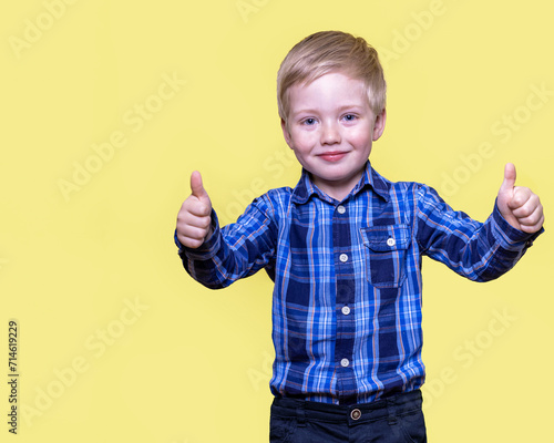 Boy holding thumbs up and smiling, yellow background with space for text