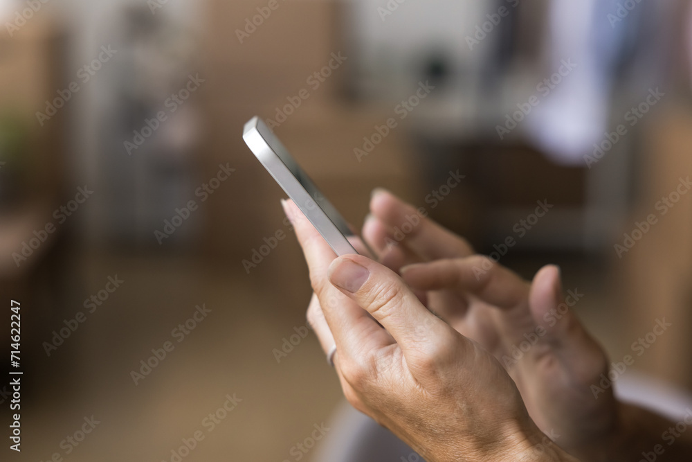 Close up shot unknown female hands holding smartphone, ordering reliable transport services on relocation day using mobile app, heap of stacked box on background. Retail electronic commerce, business