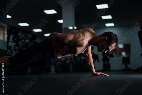 Muscular shirtless man doing one-arm push-ups in the gym. 