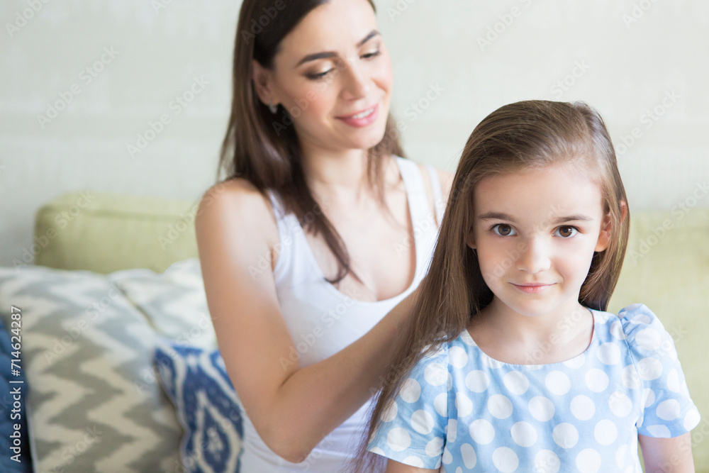 Adorable young family in living room. Mother combing her daughter's hair Adorable young family in living room. Mother combing her daughter's hair