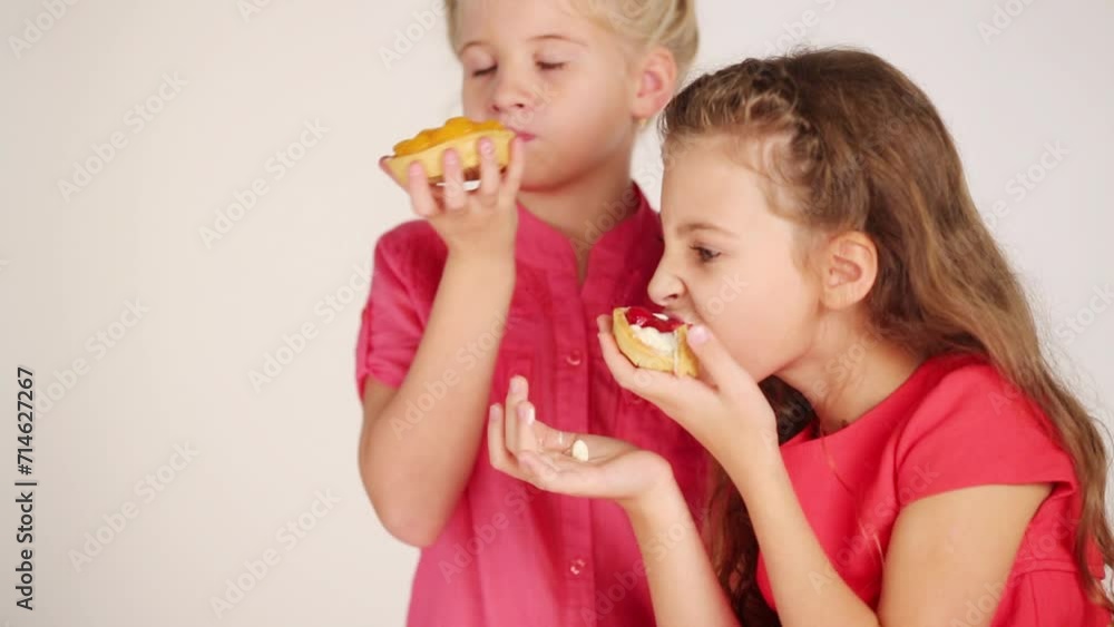 Two pretty girl eat small sweet pies in white studio Two pretty girl eat small sweet pies in white studio