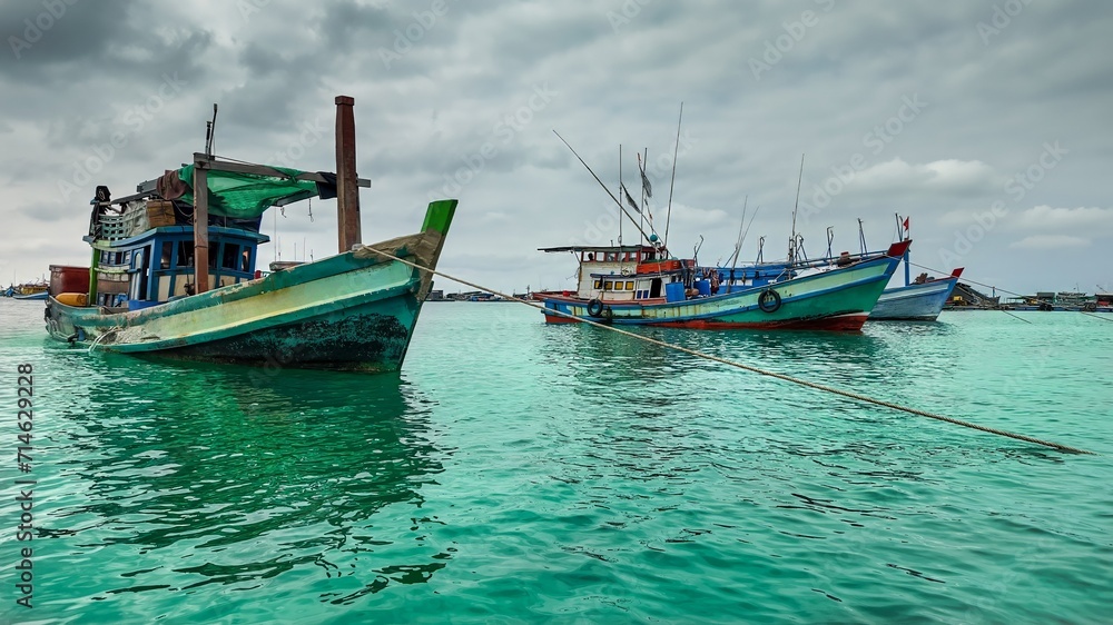 Traditional wooden fishing boats moored in tranquil turquoise waters under a cloudy sky, depicting coastal livelihoods