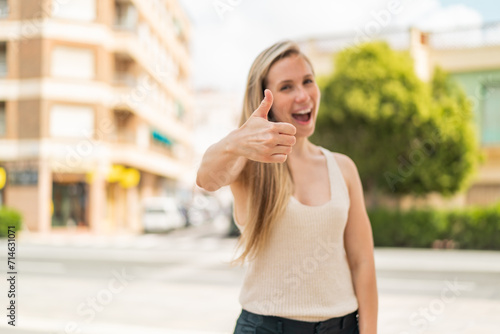 Young blonde woman at outdoors with thumbs up because something good has happened